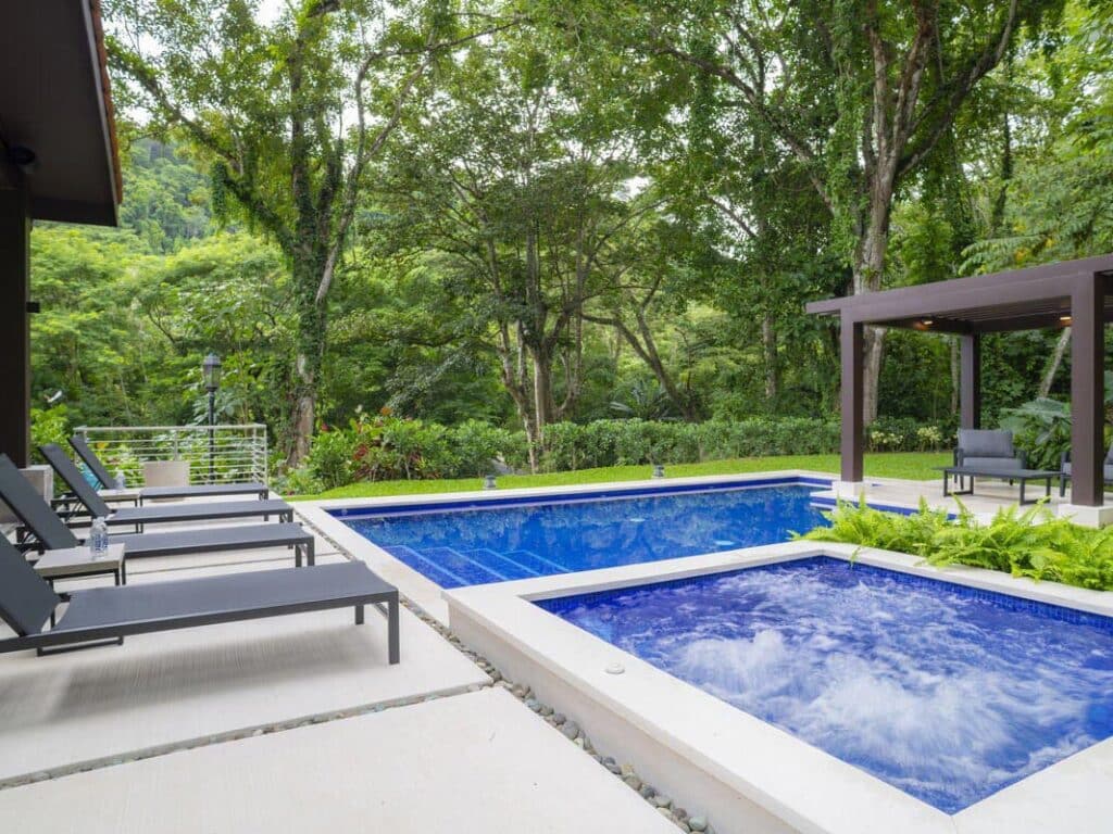 View of the outdoor patio at Casa Selva Tica featuring poolside loungers and trellis gazebo.