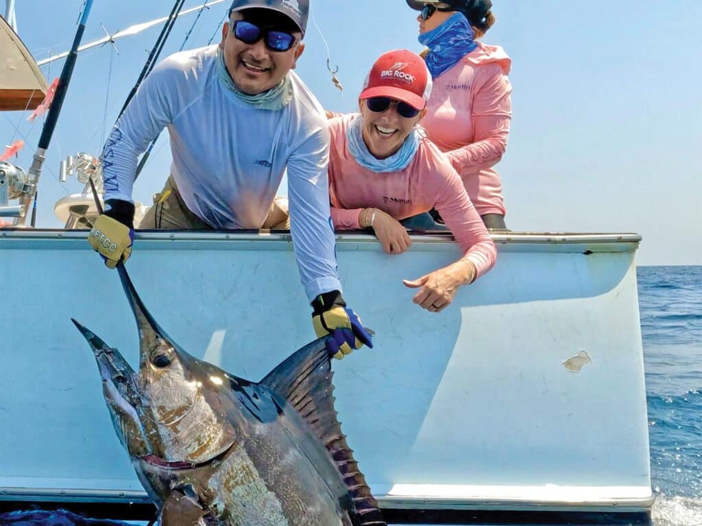 A crewmate helps an angler by pulling a large marlin boatside to pose for a photo before release.