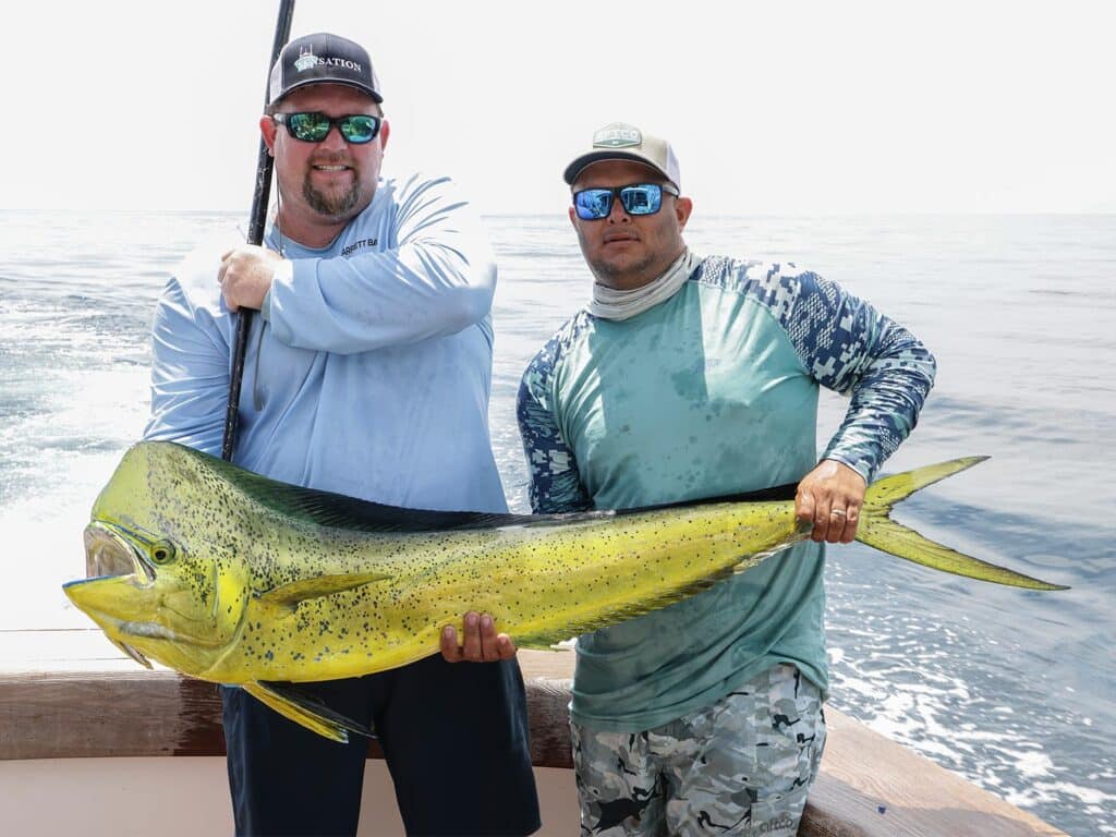 Two anglers holding up a large dorado in the cockpit of a sport-fishing boat