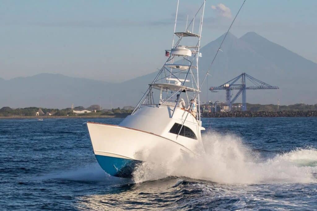 A sport-fishing boat with a blue and white hull cruises through the water.