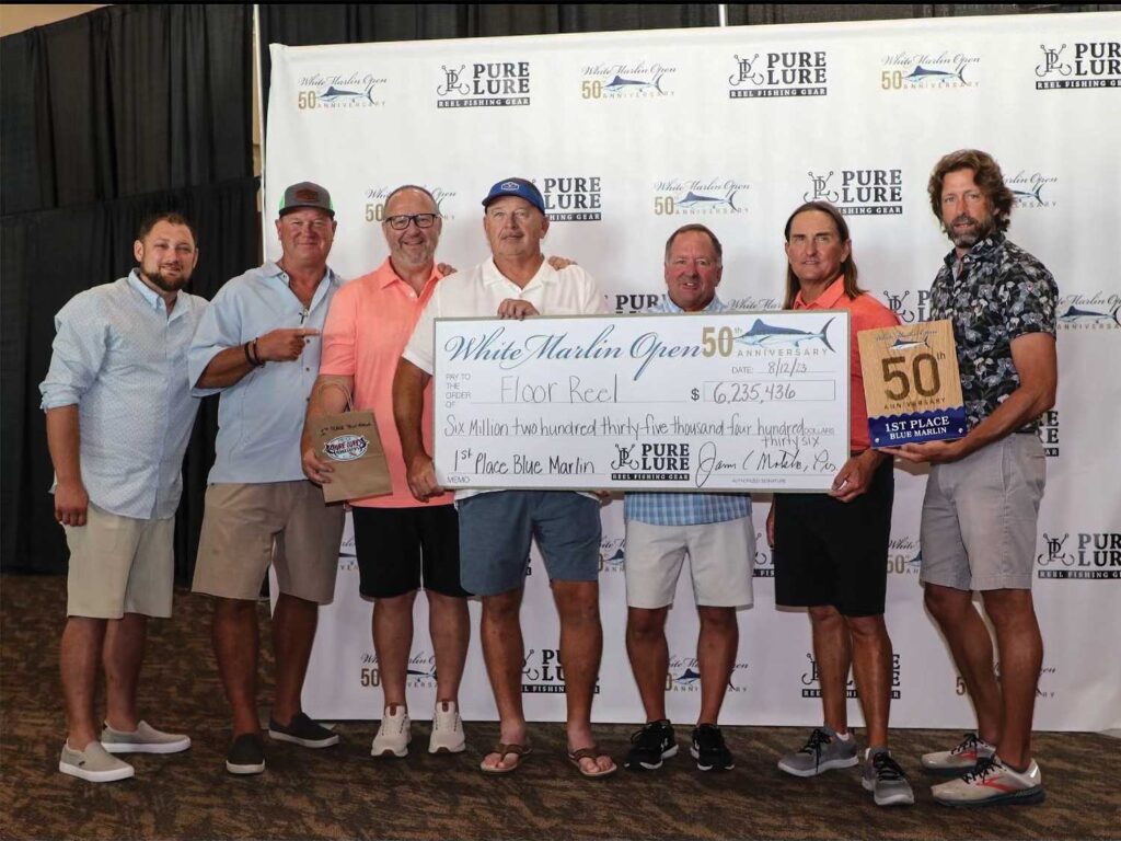 A sport-fishing team stands at an awards ceremony, holding their over-sized check.