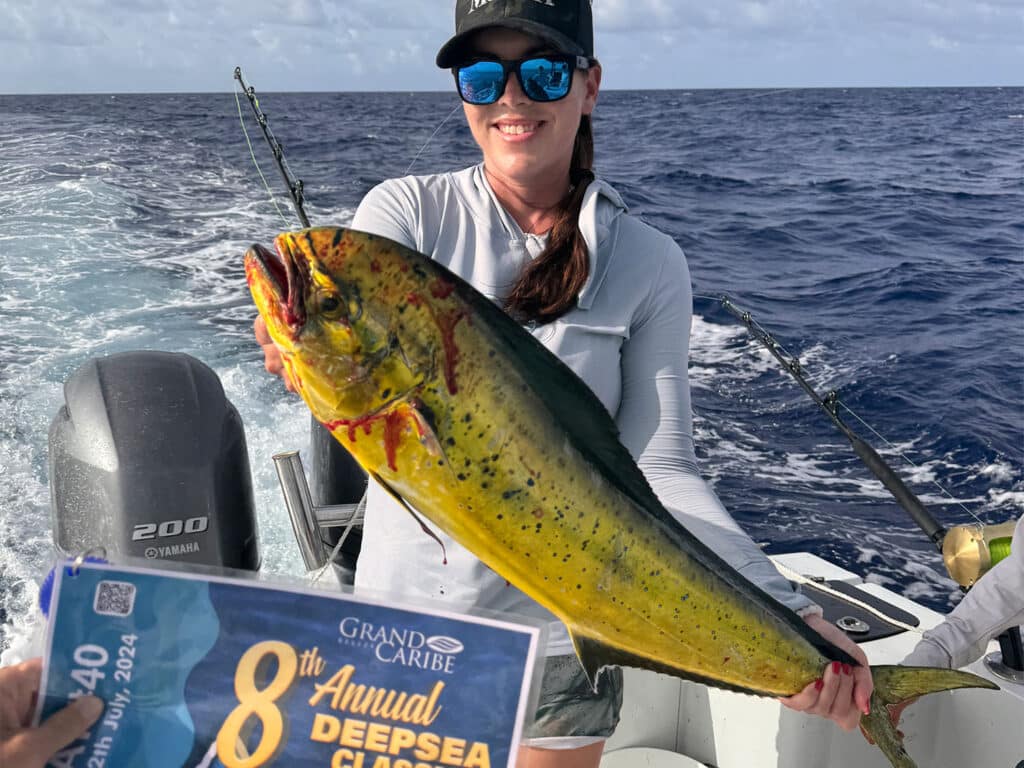 Shelby Callison holding a large dorado fish while standing in the cockpit of a sport-fishing boat.
