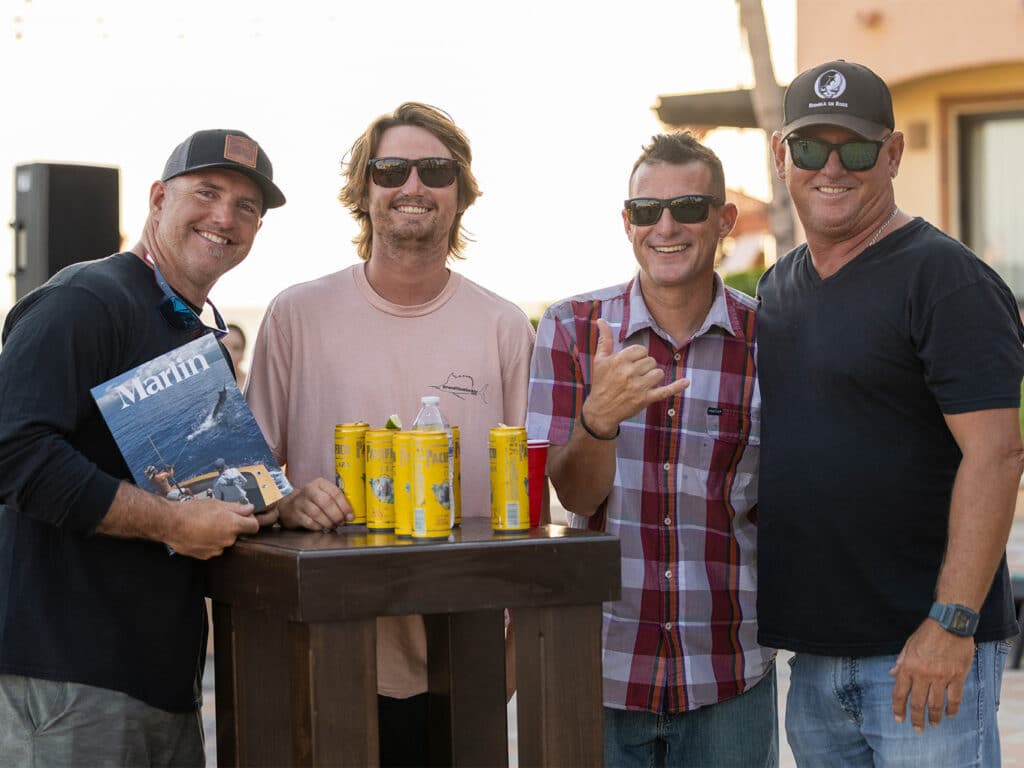 Four sport-fishing anglers stand around a table. One holds a Marlin magazine.