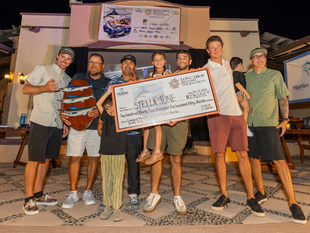 A sport-fishing team stands at an awards ceremony holding an over-sized check.