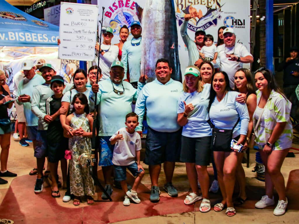 A sport-fishing team standing next to a large marlin.