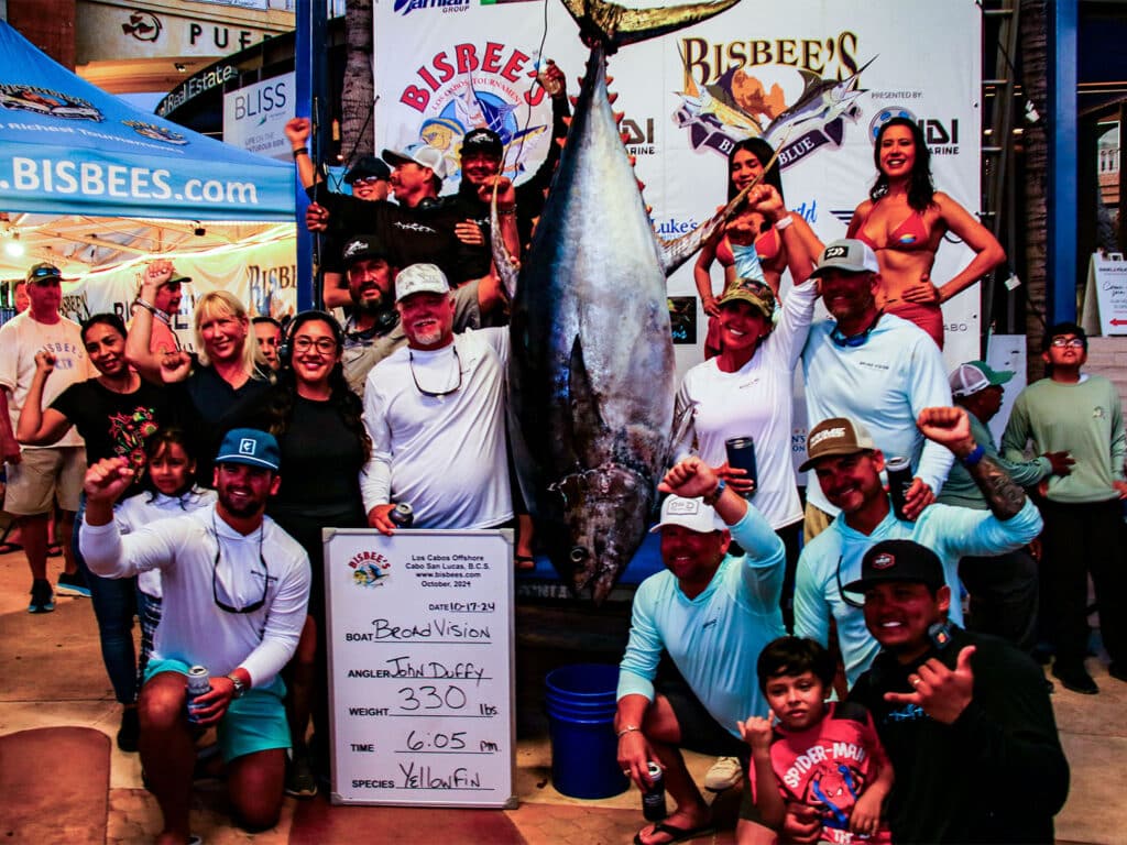 A sport-fishing team standing next to a large yellowfin tuna.