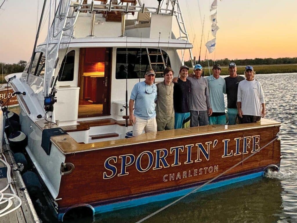 A crew of men stand in the cockpit of a sport-fishing boat.