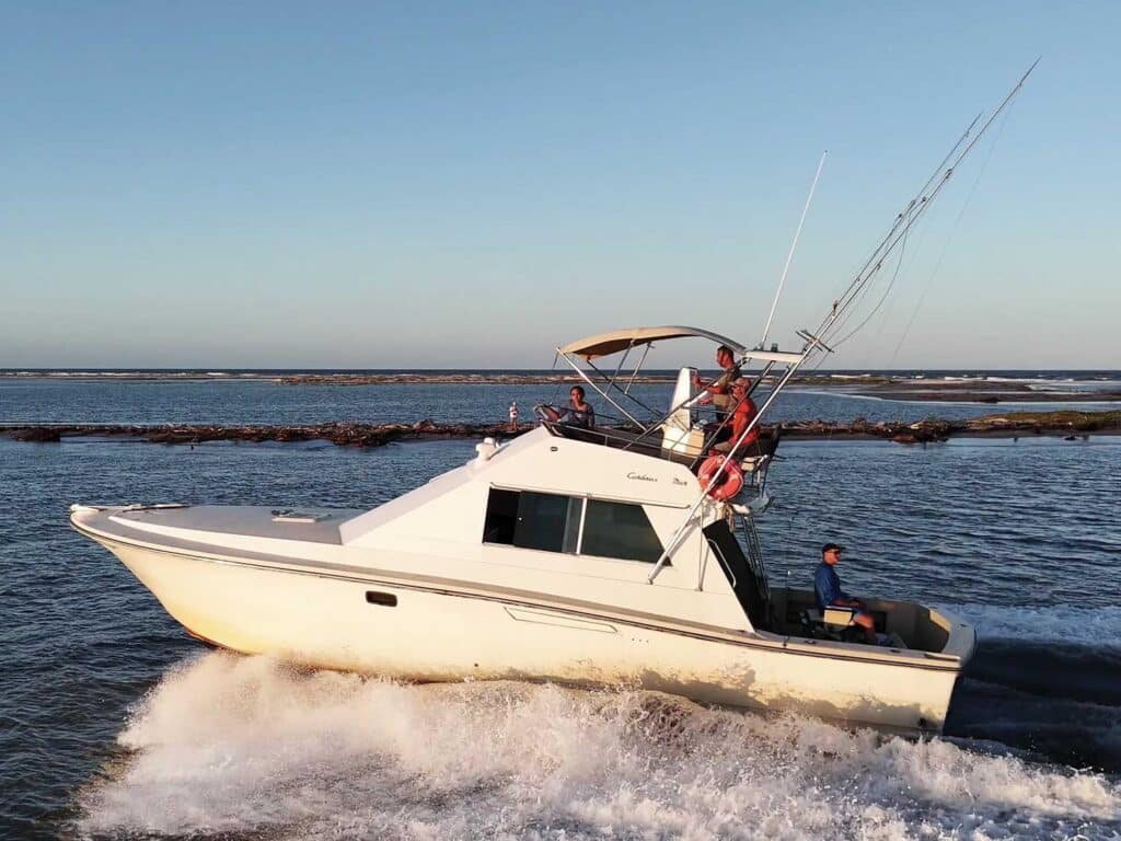 A captain pilots a sport-fishing boat past a jetty.