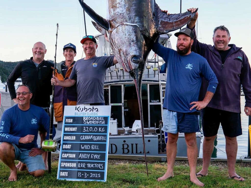 A crew of anglers stand around a large billfish being weighed.