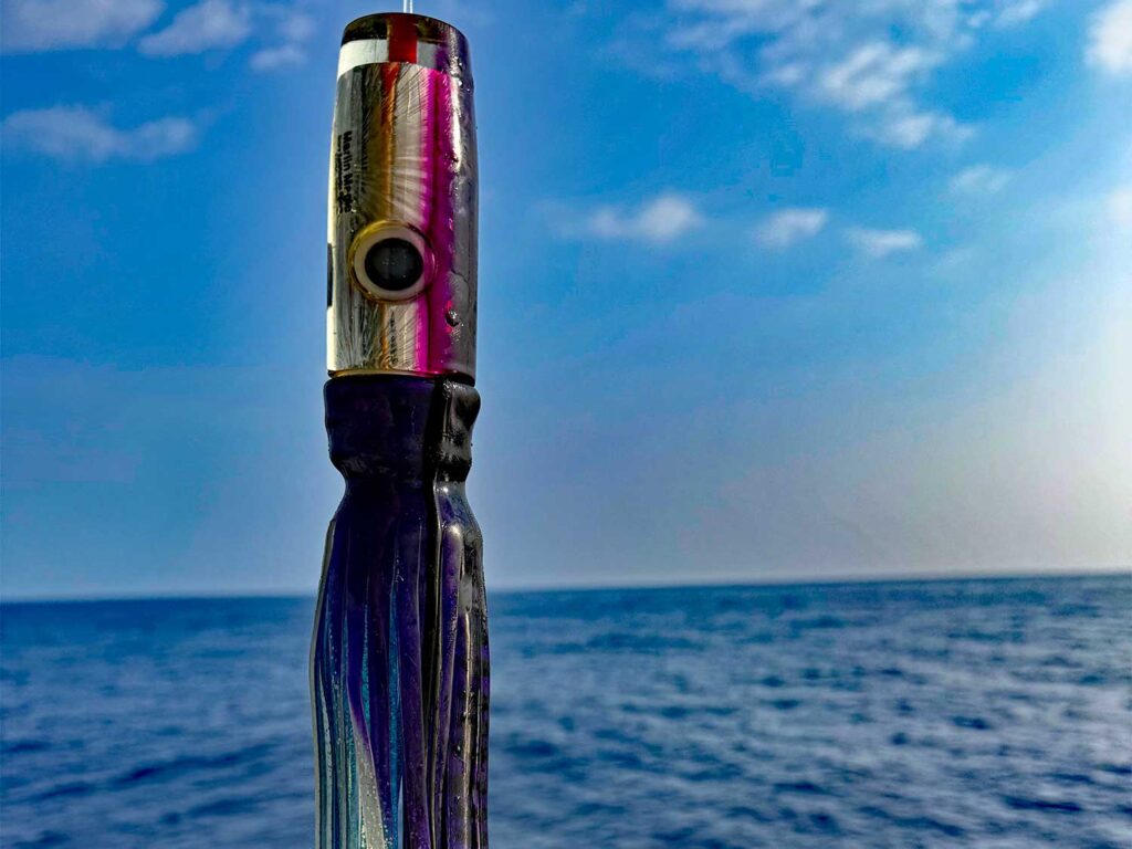 A purple Marlin Magic lure held up against the ocean horizon.