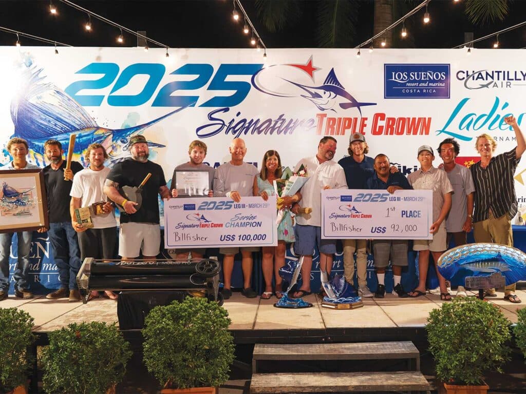 Team Billfisher stands on the award ceremony stage. They hold up prizes and over-sized checks in celebration.
