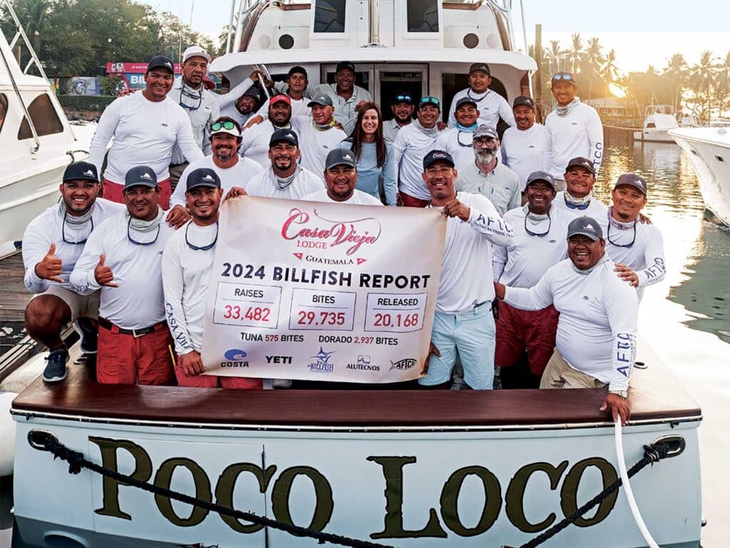 A team of anglers stand in the cockpit of a sport-fishing boat and hold up a Casa Vieja lodge sign.