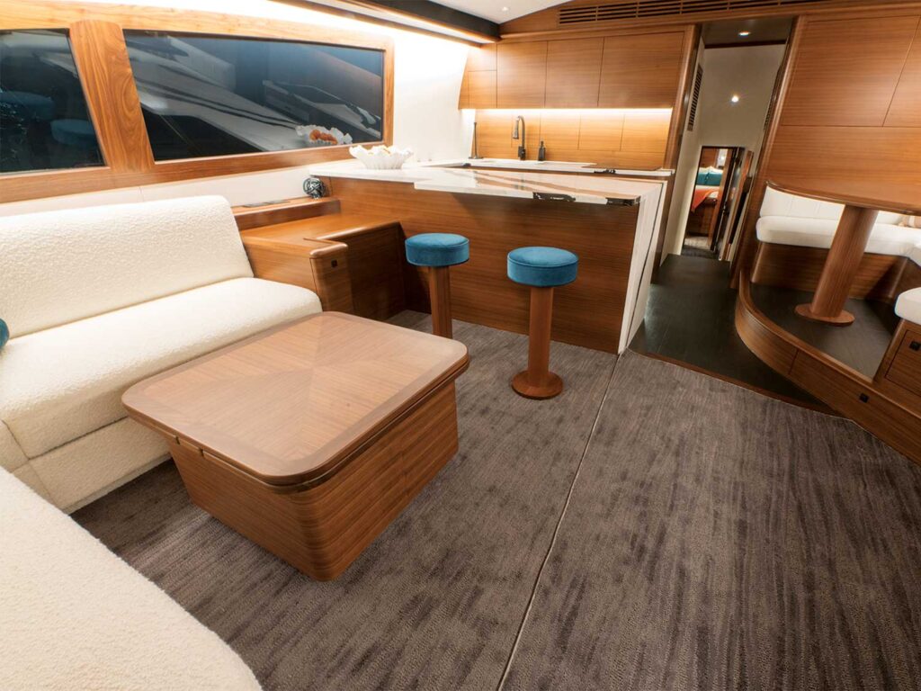 The salon and galley of a sport-fishing boat. The wood finishings are offset by white cushions and walls, with ample lighting to light the space.