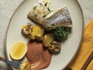 A plate of baked snapper over a bed of roasted smashed potatoees with an ahi pepper sauce.