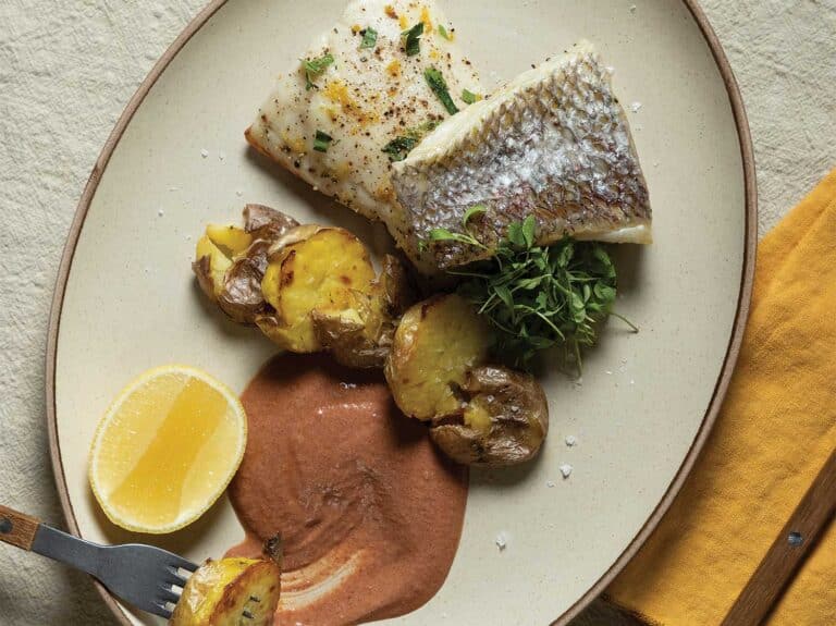 A plate of baked snapper over a bed of roasted smashed potatoees with an ahi pepper sauce.