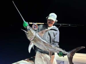An angler stands in the cockpit of a sport-fishing boat and holds up a swordfish.