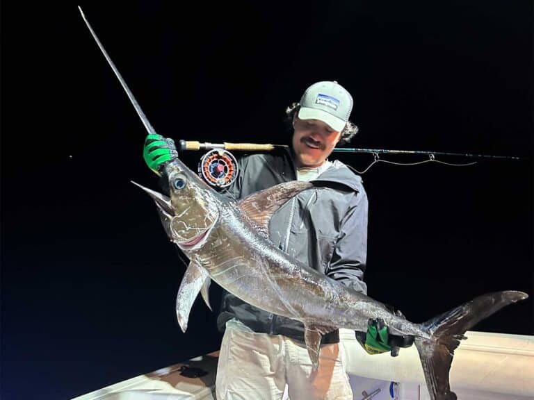 An angler stands in the cockpit of a sport-fishing boat and holds up a swordfish.