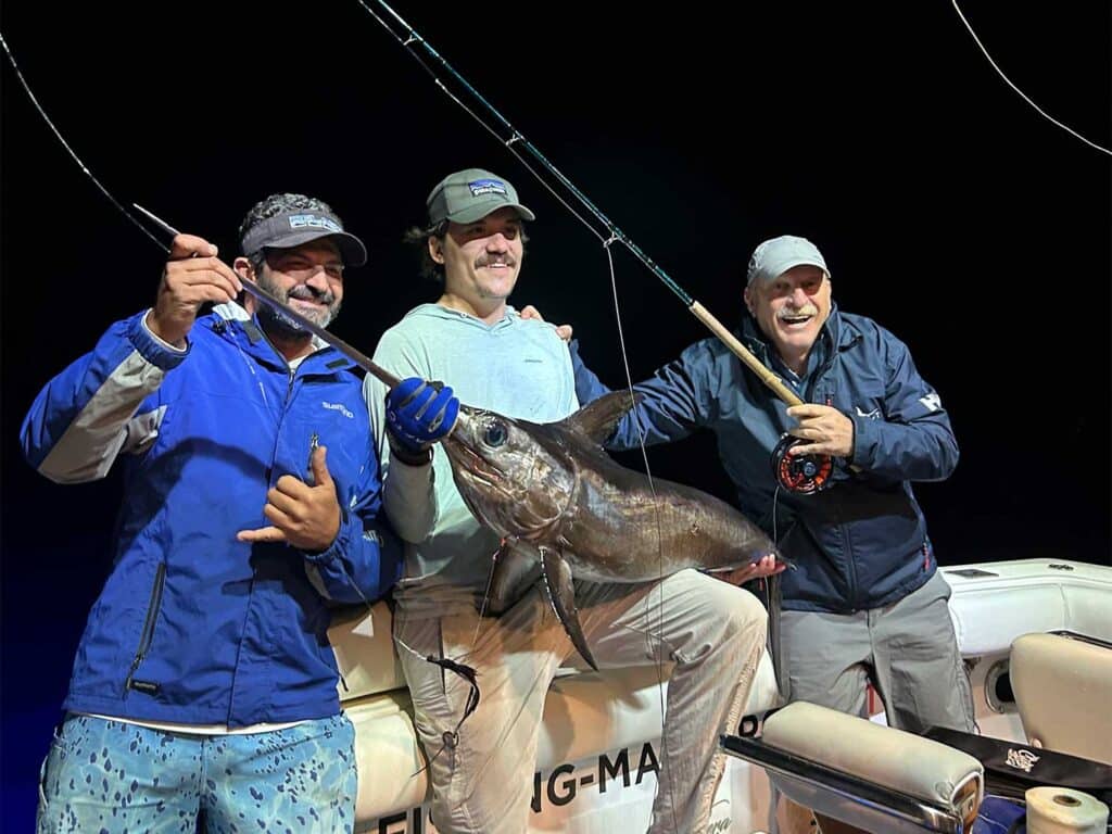 A team of three anglers pose for the camera and hold up a swordfish.