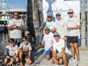 An angling team at standing next to a large blue marlin being weighed.