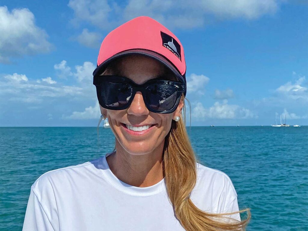 Laura Russell smiles for the camera. Clear blue ocean and clear skies are in the horizon behind her.