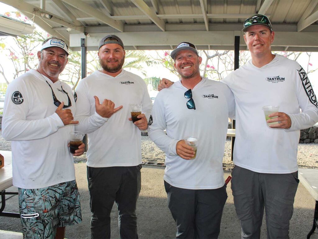 Four anglers in fishing gear stand under a covered area during a fishing tournament ceremony.