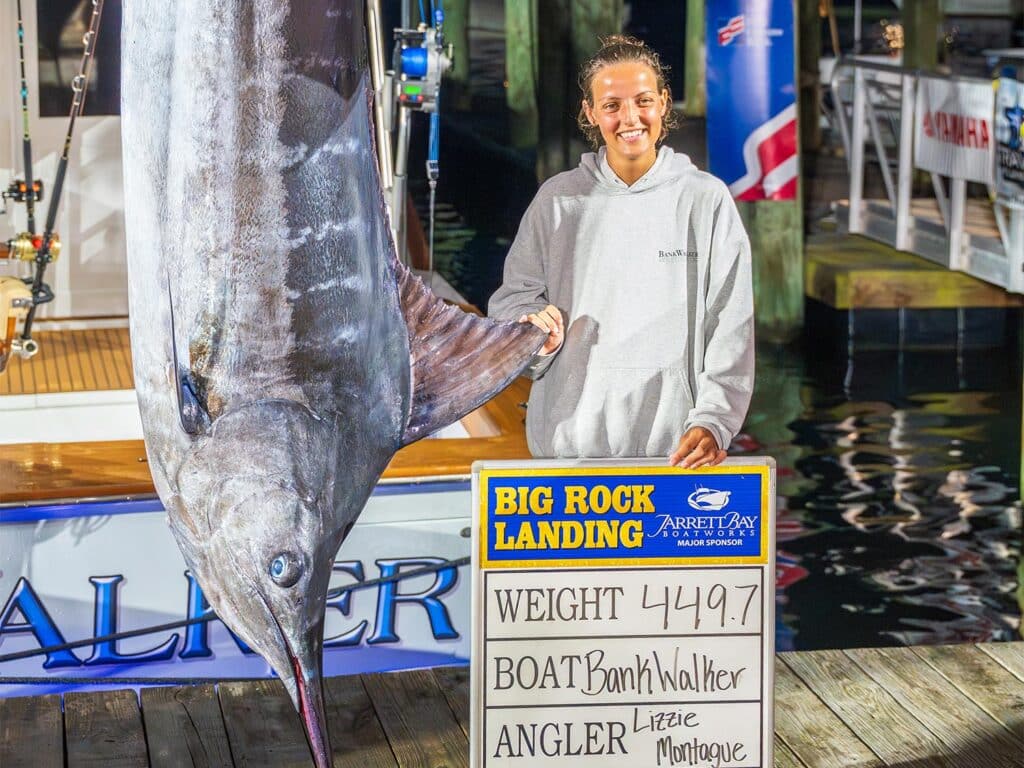 A young woman standing next to a blue marlin being weighed in.