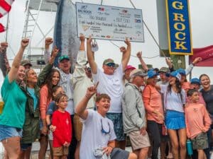 Team Big Trouble stands at the dock of the Big Rock Blue Marlin Tournament beside a weighed marlin.