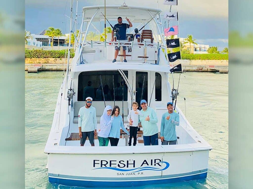 A sport-fishing crew stands in the cockpit and tower of a boat named "Fresh Air". release flags fly from the rigging.