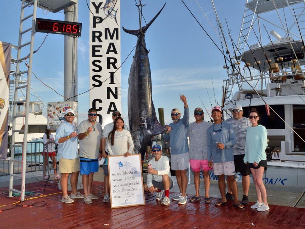 Team Rising Sons stands on the weigh-in docks nexts to their sport-fishing boat and a 618 lb blue marlin
