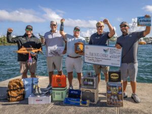 Team Builder's Choice on the docks celebrating their win. They are holding up awards, prizes, and an over-sized check.
