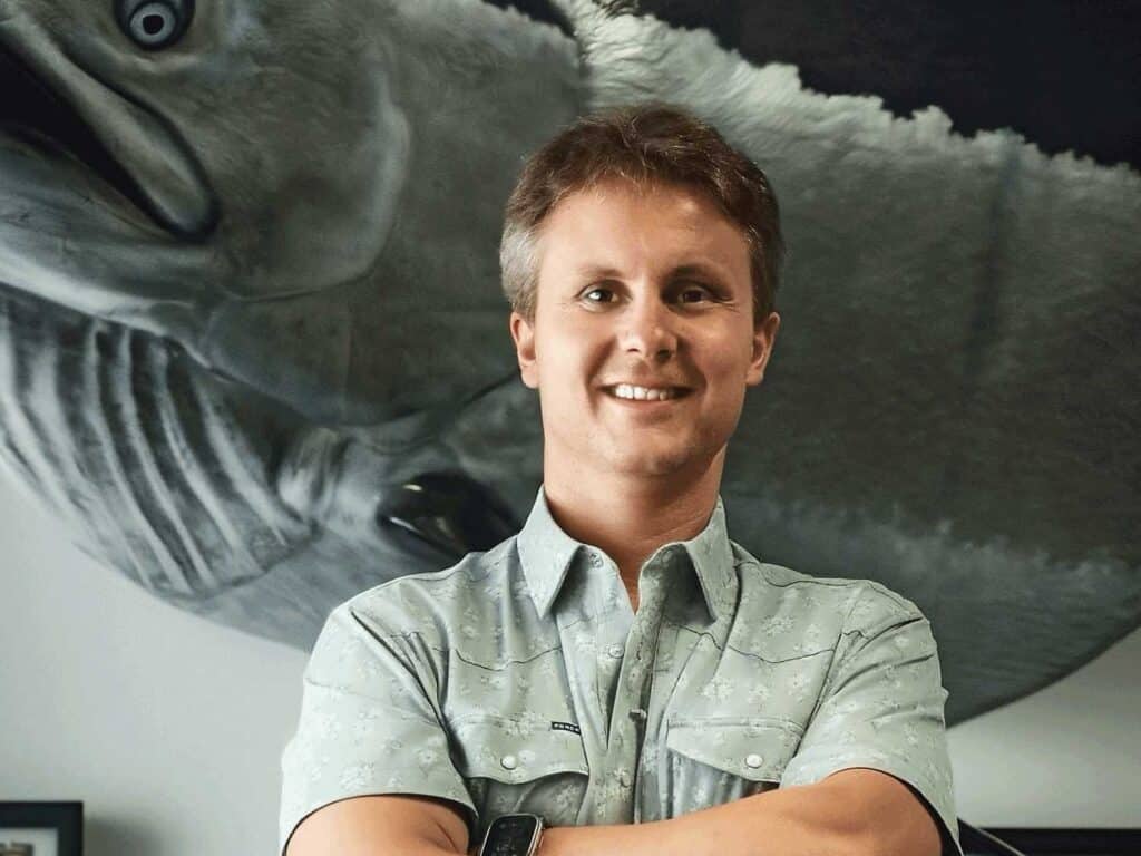Daniel Miers smiles for the camera while standing in front of a large trophy mount.