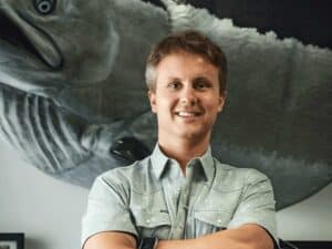 Daniel Miers smiles for the camera while standing in front of a large trophy mount.