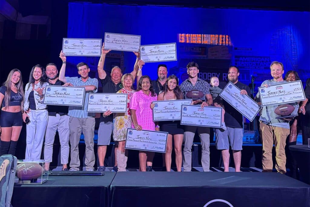 Team Jersey Nutz stands on the stage during the awards ceremony. They hold up several over-sized checks.