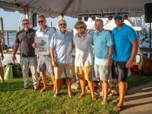 A team of anglers standing underneath a tent on a bright day.