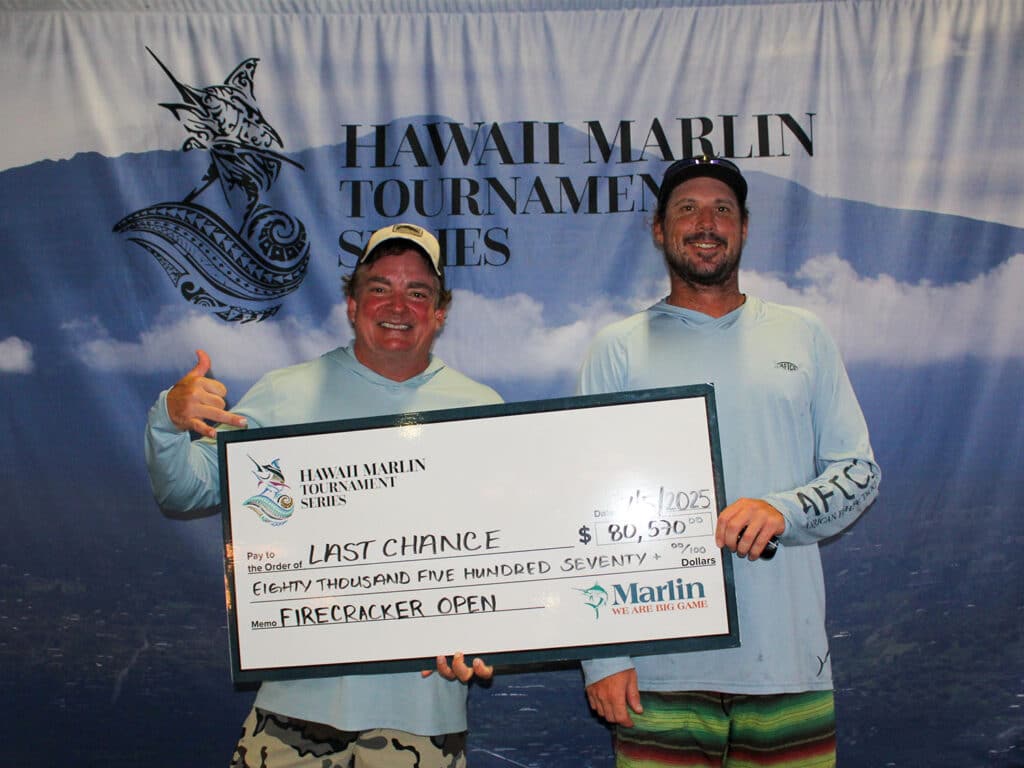 Team Last Chance stands in front of an HMTS sign at the awards ceremony and hold up their oversized check.