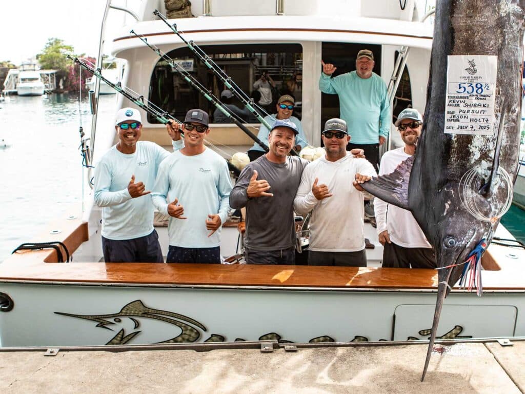Team Pursuit standing next to their large marlin being weighed dockside.