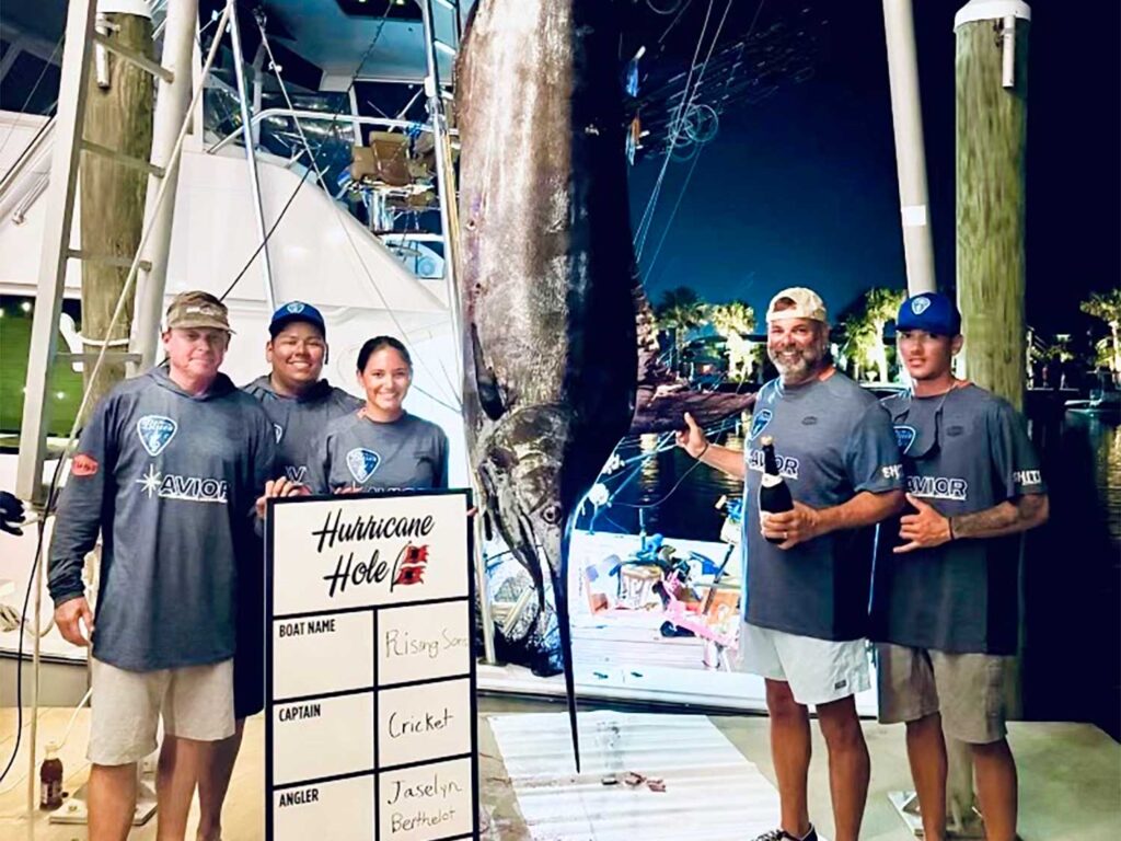 A team of anglers standing next to a large blue marlin being weighed.