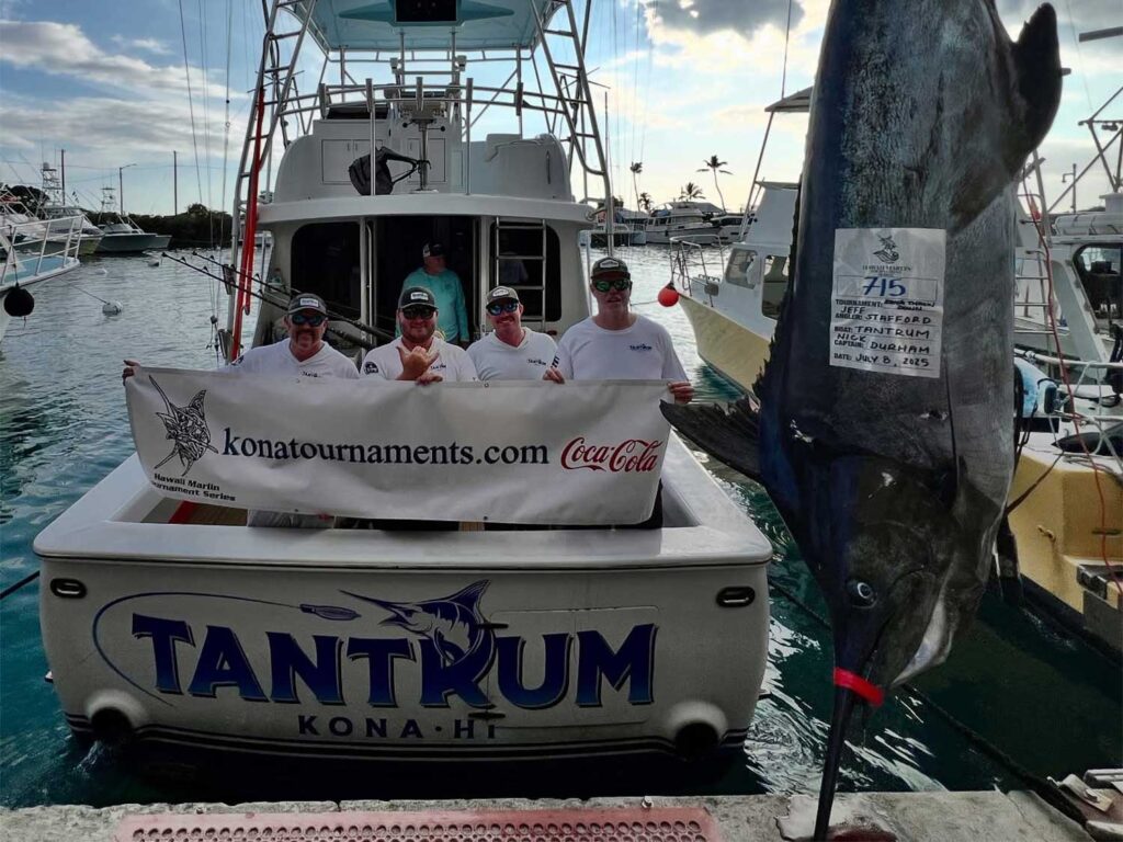 Team Tantrum stands in the cockpit of their sport-fishing boat next to a 700+ pound blue marlin being weighed dockside.