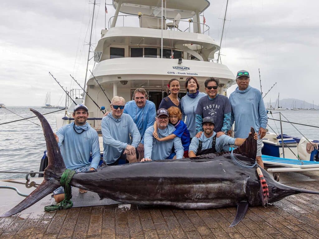 A team of anglers on a dock kneeling behind a large blue marlin on the dock in front of them.