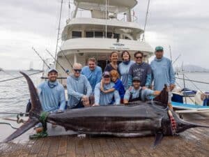 A team of anglers on a dock kneeling behind a large blue marlin on the dock in front of them.