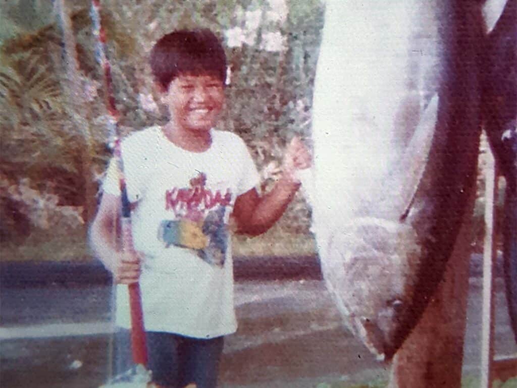Old photograph of a young Bomboy Llanes holding a fishing pole while standing next to a large tuna.