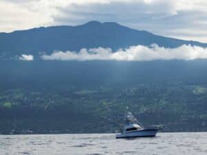 The shoreline of Hawaii. A sport-fishing boat cruises past on the ocean.