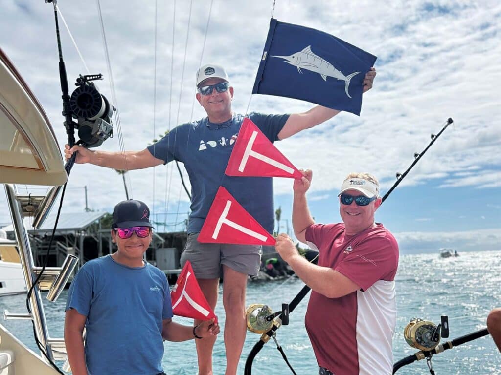 Three crew pose with release flags flying from boat rigging.
