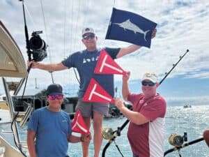 Three crew pose with release flags flying from boat rigging.