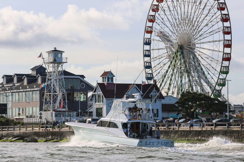 A sport-fishing boat cruises past a pier and ferris wheel.