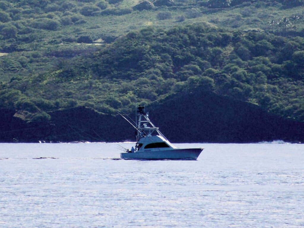 A sport-fishing boat cruises on the Kona waters. The lush Hawaii coastline can be seen in the distance.