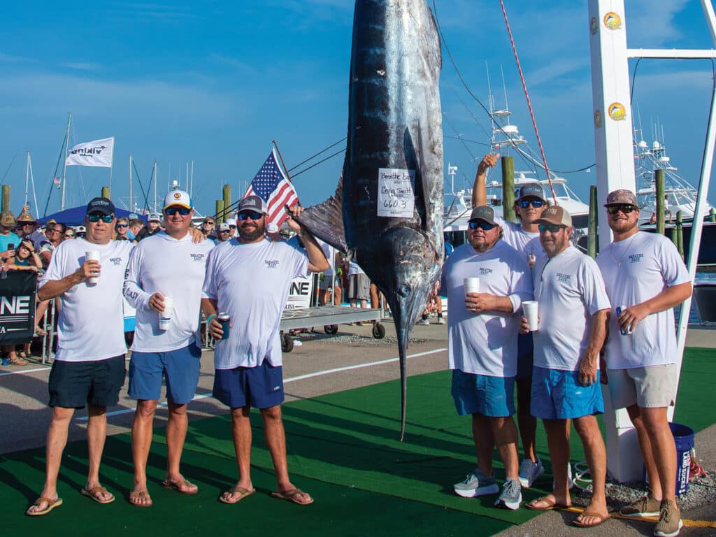A team of anglers standing beside a large marlin being weighed.