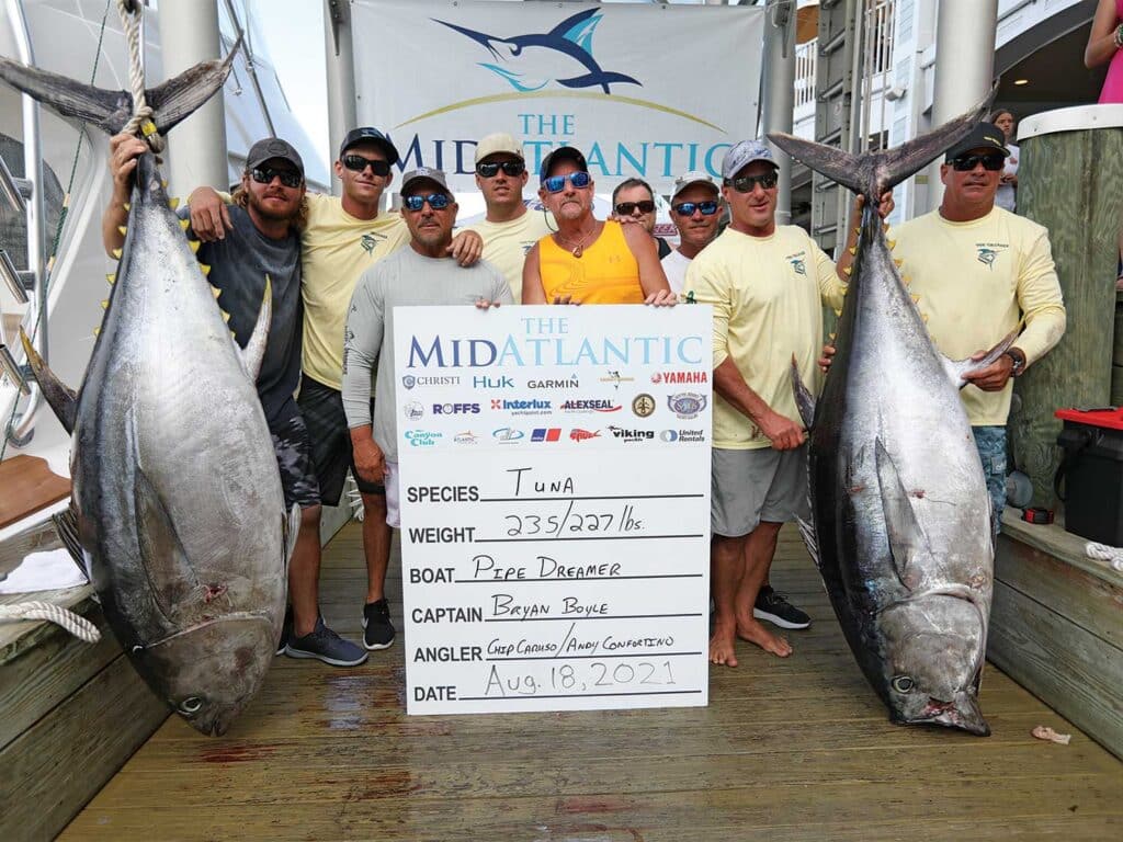 A team of anglers holding up two large tuna.